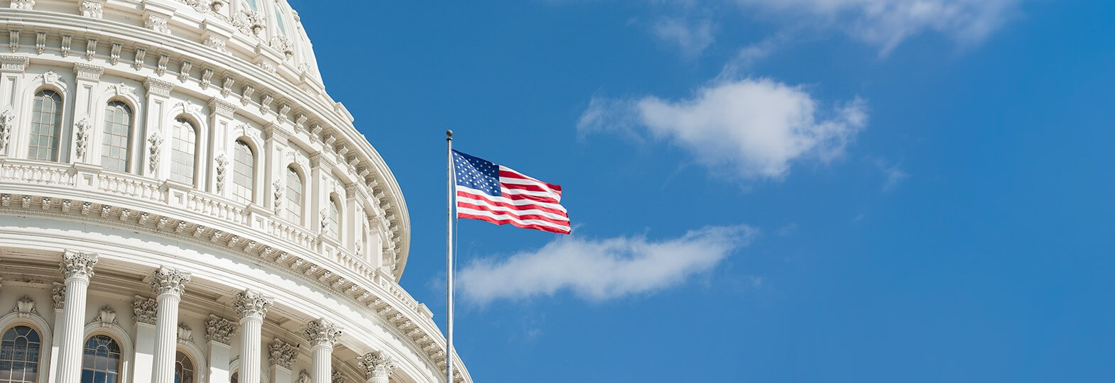 US State Capitol with USA flag pole on a mostly clear sky day
